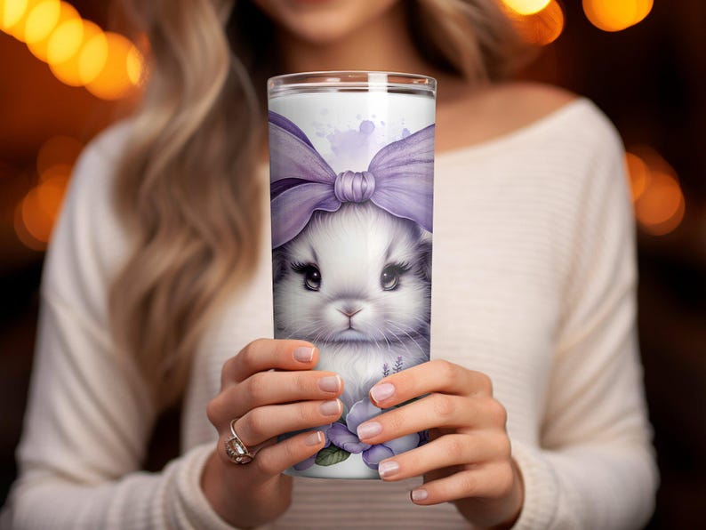 A beautiful 20 oz tumbler wrap featuring an adorable white Easter bunny with big, expressive eyes, wearing a large purple bow. Surrounded by soft pastel florals, lavender, and butterflies in a dreamy watercolor style on a white background