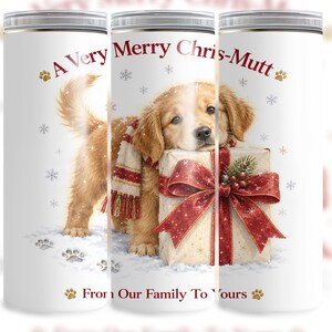 May include: A white cylindrical tumbler featuring a golden retriever puppy wearing a red and white scarf, resting its head on a gift box with a large red bow. The text reads A Very Merry Chris-Mutt and From Our Family To Yours with paw prints.