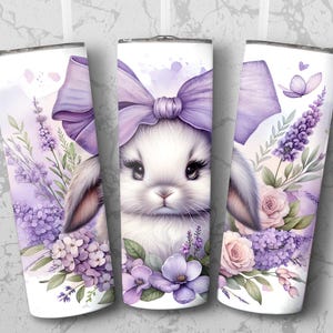 A beautiful 20 oz tumbler wrap featuring an adorable white Easter bunny with big, expressive eyes, wearing a large purple bow. Surrounded by soft pastel florals, lavender, and butterflies in a dreamy watercolor style on a white background