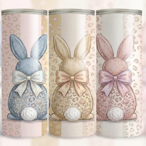 Puede incluir: Tres vasos decorativos con diseños de conejos. Cada vaso tiene una combinación de colores diferente: azul, beige y rosa. Los conejos tienen lazos y estampados florales. El fondo tiene un estampado de leopardo.