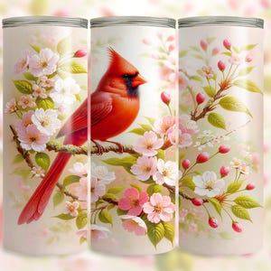 May include: A tumbler featuring a vibrant red cardinal perched on a branch adorned with delicate pink and white blossoms. The design is set against a soft, cream-colored background, creating a serene and nature-inspired aesthetic.
