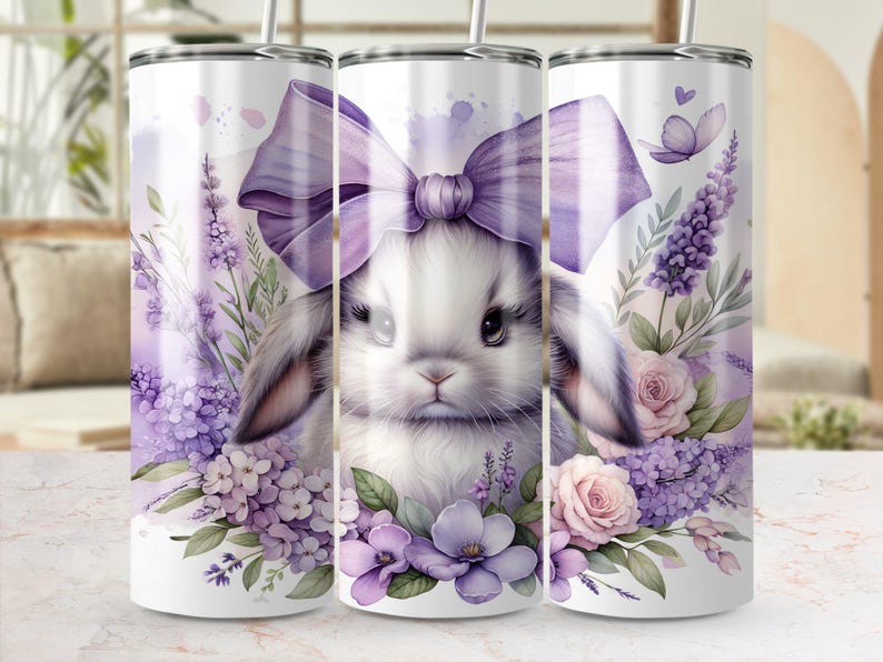 A beautiful 20 oz tumbler wrap featuring an adorable white Easter bunny with big, expressive eyes, wearing a large purple bow. Surrounded by soft pastel florals, lavender, and butterflies in a dreamy watercolor style on a white background