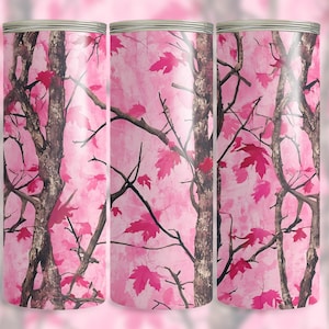 May include: A set of three cylindrical tumblers with a pink camouflage design. The pattern features tree branches and pink maple leaves against a pink background. The tumblers have a silver rim.