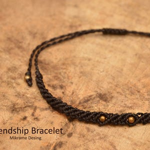Puede incluir: Pulsera de la amistad negra con tres cuentas doradas. La pulsera está hecha con un cordón trenzado y está atada con un nudo en el extremo.