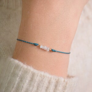 Puede incluir: Un brazalete de cuerda azul turquesa con pequeñas cuentas de piedras preciosas blancas.