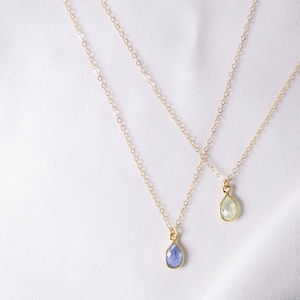 May include: Two gold necklaces with teardrop-shaped gemstone pendants. One pendant is a light blue colour, and the other is a light green colour.