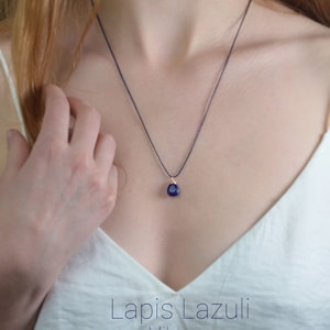 May include: A dark blue Lapis Lazuli gemstone pendant on a black cord necklace. The necklace is worn by a person with long blonde hair. The text "Lapis Lazuli Mikrame Healing Jewelry" is at the bottom of the image.