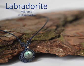 May include: A dark blue macrame necklace with a labradorite gemstone pendant. The necklace is displayed on a piece of tree bark.