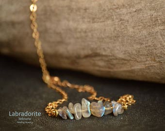 May include: A gold chain necklace with a row of iridescent labradorite stones. The stones are faceted and have a shimmery, opalescent quality. The necklace is delicate and feminine.
