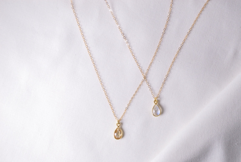 May include: Two gold necklaces with teardrop-shaped pendants. The pendants are clear and have a slight iridescent shimmer.