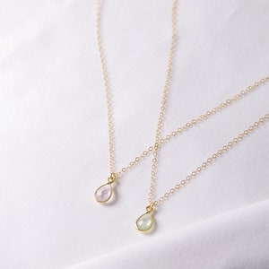 Puede incluir: Dos collares de cadena de oro con colgantes en forma de l&aacute;grima. El colgante superior es de color rosa claro y el colgante inferior es de color verde claro.