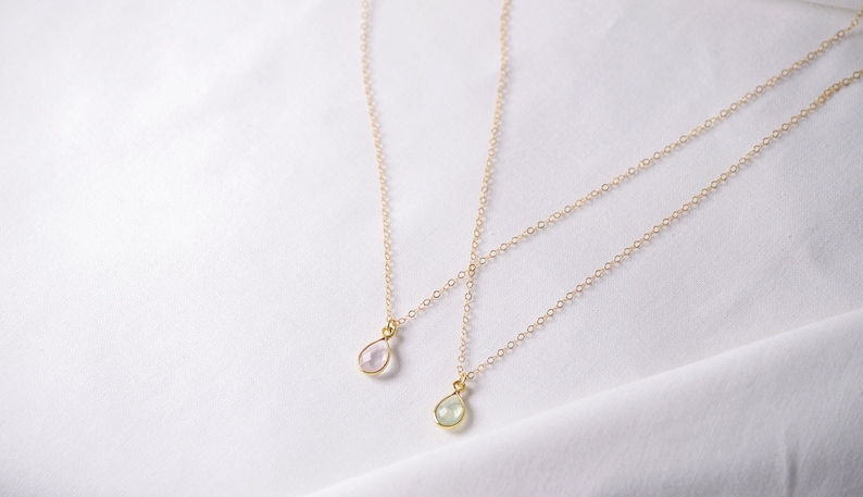 Puede incluir: Dos collares de cadena de oro con colgantes en forma de l&aacute;grima. El colgante superior es de color rosa claro y el colgante inferior es de color verde claro.