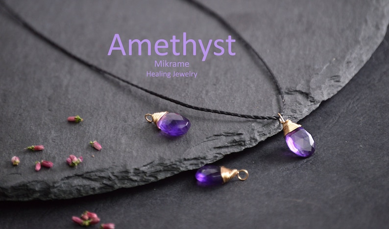 May include: Amethyst necklace with three purple gemstone pendants wrapped in gold wire. The necklace is on a black cord and is displayed on a dark grey slate surface. The text "Mikrame Healing Jewelry" is visible below the word "Amethyst".