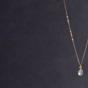 May include: A gold chain necklace with a teardrop-shaped blue gemstone pendant.