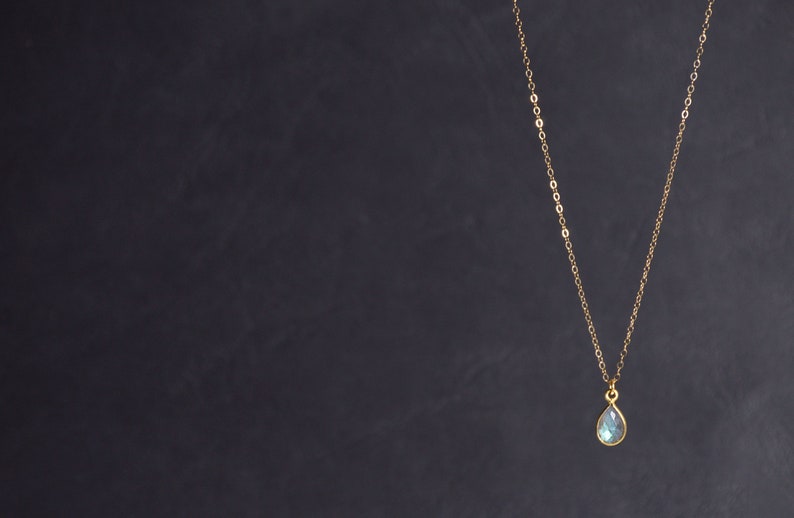 May include: A gold chain necklace with a teardrop-shaped blue gemstone pendant.