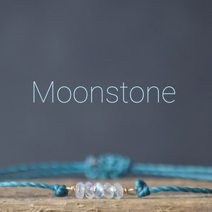 May include: A teal blue string bracelet with a gold accent and a row of moonstone beads.