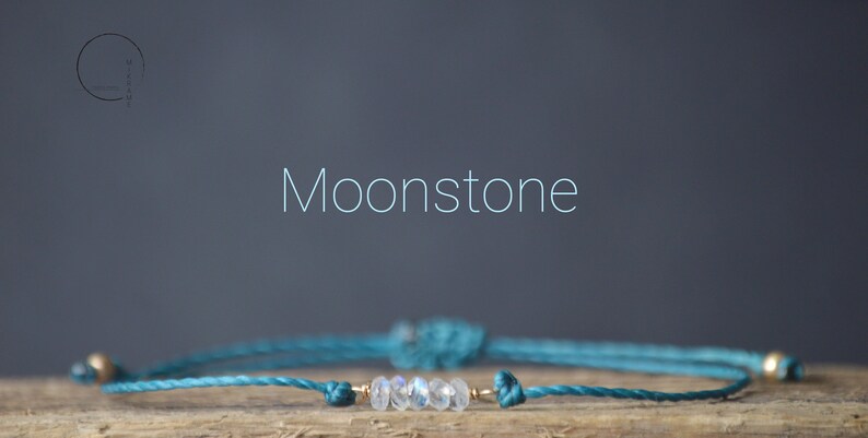 May include: A teal blue string bracelet with a gold accent and a row of moonstone beads.