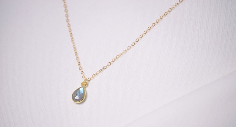 May include: A delicate gold chain necklace with a teardrop-shaped labradorite gemstone pendant.