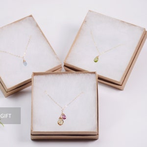 May include: Three delicate gold necklaces with gemstone pendants in a brown gift box. The necklaces feature a light blue gemstone, a green gemstone, and a yellow gemstone with a pink gemstone accent. The boxes are labeled "READY TO GIFT".