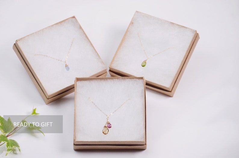 May include: Three delicate gold necklaces with gemstone pendants in a brown gift box. The necklaces feature a light blue gemstone, a green gemstone, and a yellow gemstone with a pink gemstone accent. The boxes are labeled "READY TO GIFT".