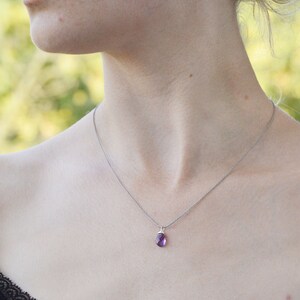 May include: A silver chain necklace with a small, purple gemstone pendant. The necklace is worn by a person with a black lace top.