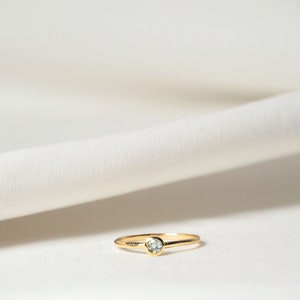 Puede incluir: Un delicado anillo de oro con una pequeña piedra preciosa azul claro engastada en el centro.