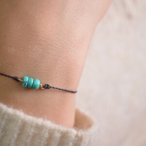 May include: A simple bracelet with a black cord and three turquoise beads.