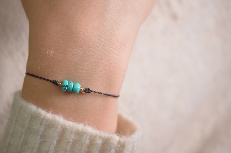 May include: A simple bracelet with a black cord and three turquoise beads.