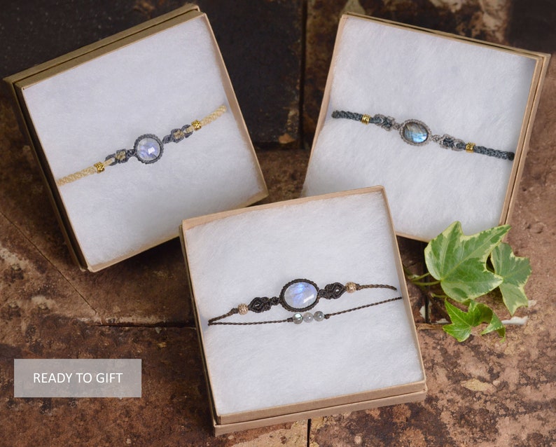 May include: Three gift boxes with white interior and brown exterior, each containing a different moonstone bracelet. The bracelets are made with brown cord and feature a moonstone gemstone. The boxes are sitting on a brown textured surface.  READY TO GIFT.