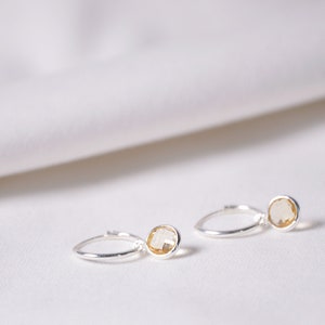 Op de afbeelding: Een paar zilveren oorringen met kleine, ronde, gele edelstenen.
