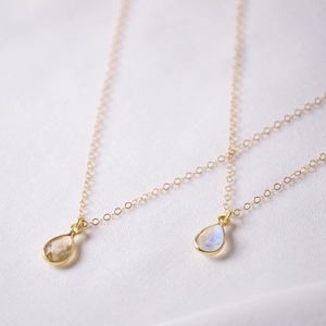 May include: Two gold necklaces with teardrop-shaped moonstone pendants. The necklaces are on a white background.