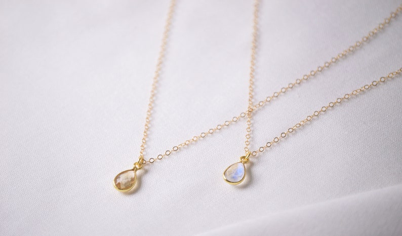 May include: Two gold necklaces with teardrop-shaped moonstone pendants. The necklaces are on a white background.
