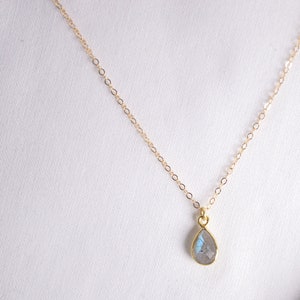 May include: A delicate gold chain necklace with a teardrop-shaped pendant featuring a clear iridescent gemstone.