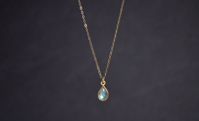 May include: A gold chain necklace with a teardrop-shaped pendant featuring a light blue and green gemstone.