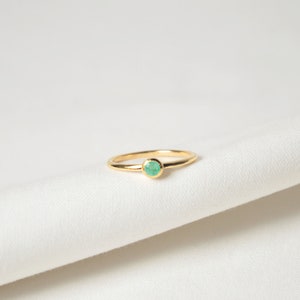 Puede incluir: Un anillo de oro con una sola piedra preciosa redonda de color verde claro.