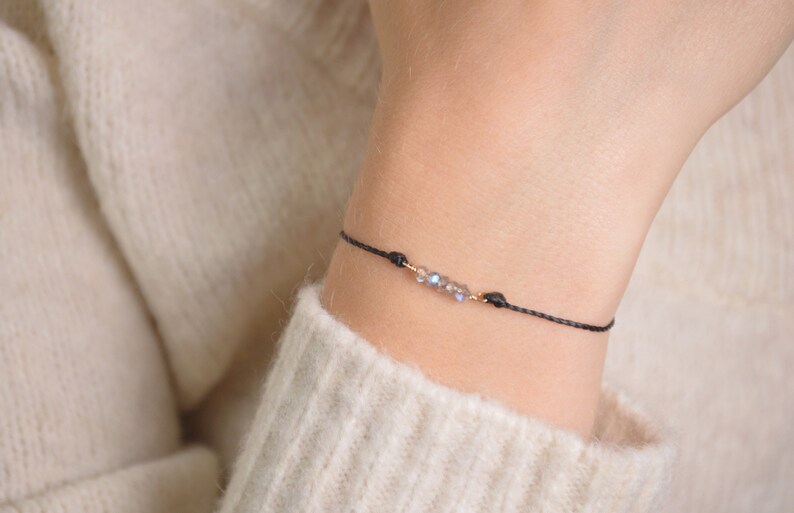 May include: A delicate black string bracelet with a small cluster of iridescent crystals and gold accents.