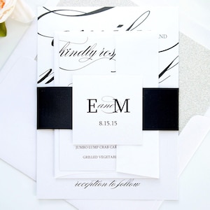 May include: Elegant wedding invitation suite with a white and black color scheme. The invitation features calligraphy, a black band, and the initials "E and M" with the date 8.15.15. A white envelope and a light pink flower are also visible.