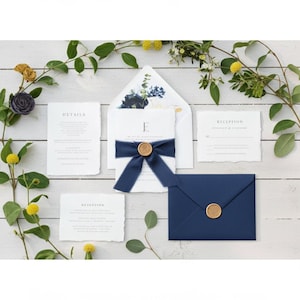 Elegant wedding invitation suite featuring a navy blue envelope with a gold wax seal, invitation cards, and a card with the word "DETAILS". The invitation is tied with a navy blue ribbon and a gold seal.