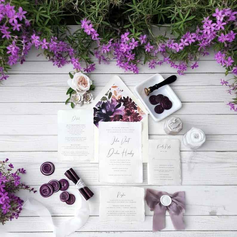 Wedding invitation suite with floral envelope, stationery, and purple wax seals. The suite includes invitation cards, RSVP cards, and a ribbon with a wax seal.