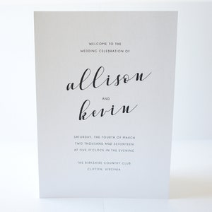 May include: A white wedding sign with black calligraphy text. The sign reads "Welcome to the Wedding Celebration of Allison and Kevin." Additional text includes the date, time, and location of the event.