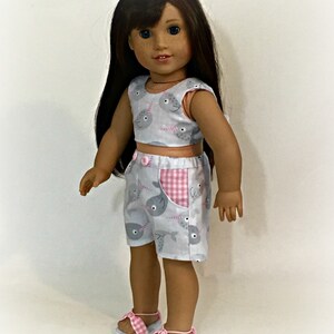 May include: A doll wearing a gray and pink outfit with a narwhal print. The outfit includes a sleeveless top and shorts. The doll is wearing pink sandals with white straps. The text "Sew Dolled Up 81" is visible at the bottom of the image.