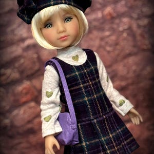 May include: A doll with blonde hair wearing a dark purple and green plaid beret, a white long-sleeve shirt with small green heart prints, and a matching plaid jumper dress. A small purple shoulder bag is worn across the body. Text reads Sew Dolled Up 81.
