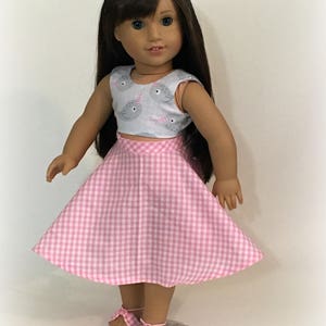 May include: A doll wearing a pink and white gingham skirt and a sleeveless top with a narwhal print. The doll has brown hair and blue eyes. The text "Sew Dolled Up 81" is at the bottom of the image.
