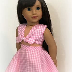 May include: A pink and white gingham doll dress with a matching top. The top has a bow tie detail. The doll is wearing the dress and has long brown hair. The text "Sew Dolled Up 81" is at the bottom of the image.