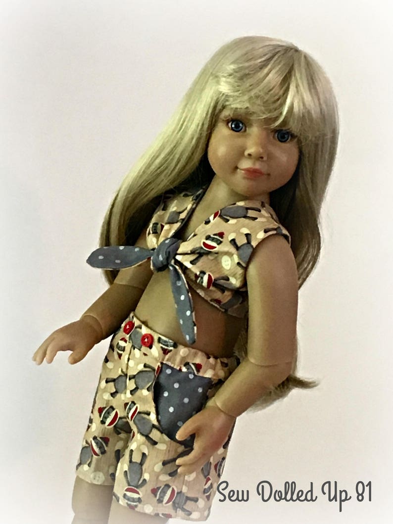 May include: A doll wearing a beige and brown sleeveless top with a blue and white polka dot tie, and matching shorts with a blue and white polka dot pocket. The doll has long blonde hair and blue eyes. The text "Sew Dolled Up 81" is visible in the bottom right corner of the image.