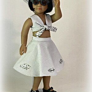 May include: A white doll wearing a white polka dot crop top with a black bow, a white polka dot skirt with black designs, a white hat, and black sunglasses. The doll is standing on a white stand. The text "Sew Dolled Up 81" is at the bottom of the image.
