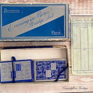 May include: A vintage "Evening in Paris" bridge set in a blue and white box. The set includes two decks of cards, a score tablet, and a box with the text "Bourjois Paris". The cards and box have a blue and white design.