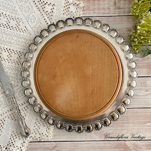 May include: A silver-edged wooden serving tray with a decorative border of square accents. A silver knife with an ornate handle rests on a white lace tablecloth. The tray has a light brown wooden centre.