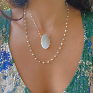 May include: A layered necklace with a large oval white stone pendant and a smaller chain of white beads.