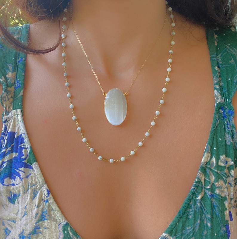May include: A layered necklace with a large oval white stone pendant and a smaller chain of white beads.